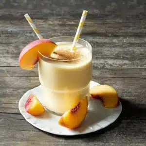 Glass of creamy peach smoothie with cinnamon on top—easy homemade metabolism booster smoothie recipe.