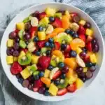 Colorful summer fruit salad with fresh orange juice, pineapple, kiwi, strawberries, green grapes, and honey drizzle