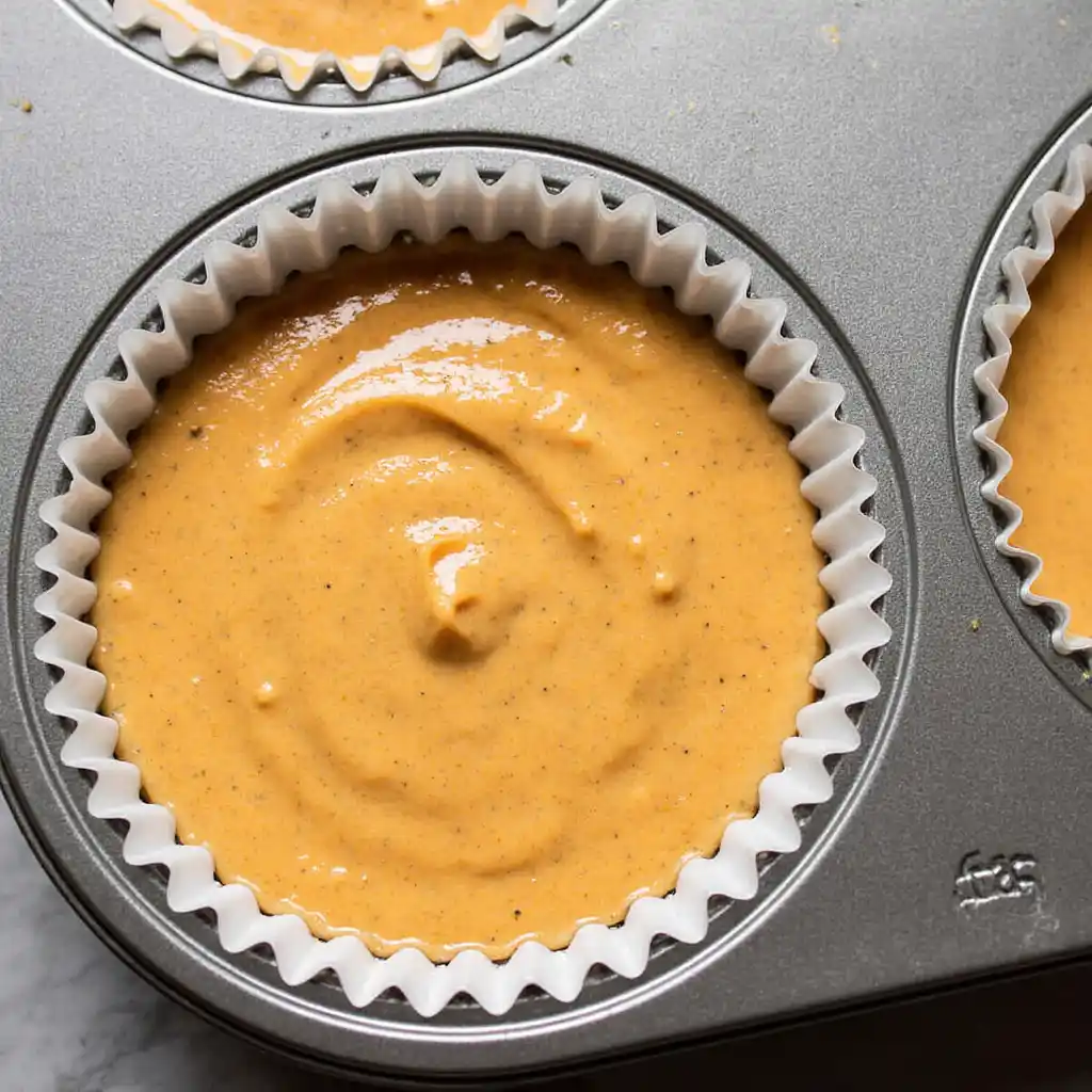 Pumpkin cheesecake batter in muffin liners for mini cranberry pumpkin cheesecakes.